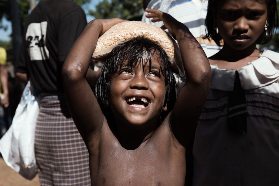 Boy Carrying a Bag of Grain, Bangladesh: a laughing boy with wet hair balancing a bag of grain on his head, looking up. Photograph by Marcus Vallance. Photograph of the week, The Guardian.