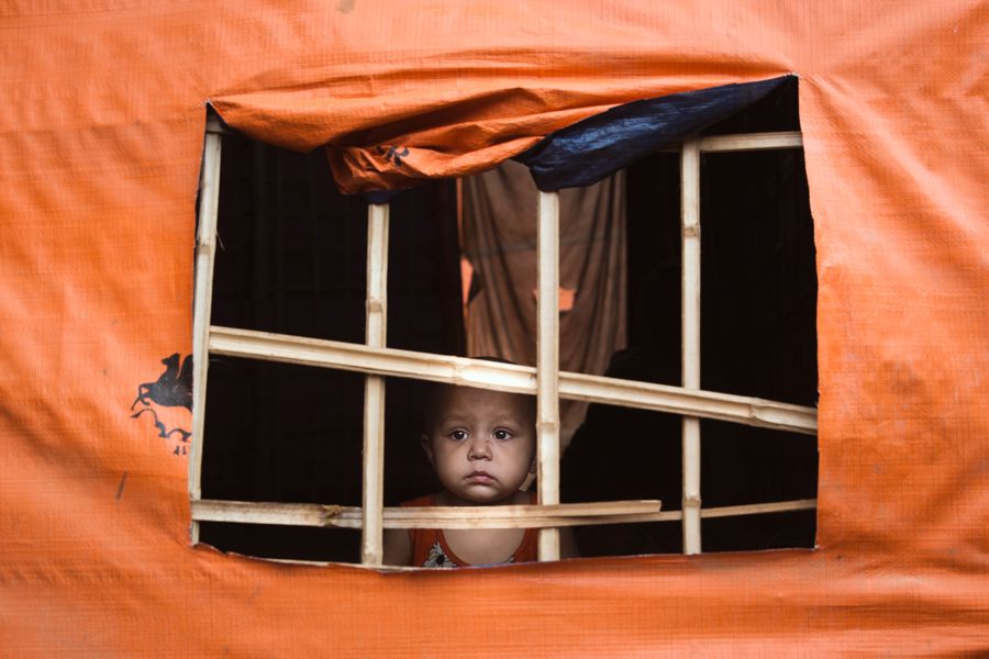 Child at a Window, Kutupalong Refugee Camp, Bangladesh: a small child looking out through the bamboo frame of a window cut in an orange tarpaulin shelter. Photograph by Marcus Vallance. Shortlisted, Documentary, British Photography Awards.