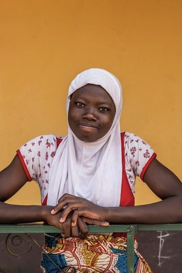 Portrait of a Girl, Tamale, Ghana: a girl with tribal marks on her cheeks, in a white headscarf, leaning on a railing in front of a yellow wall near Tamale. Photograph by Marcus Vallance.