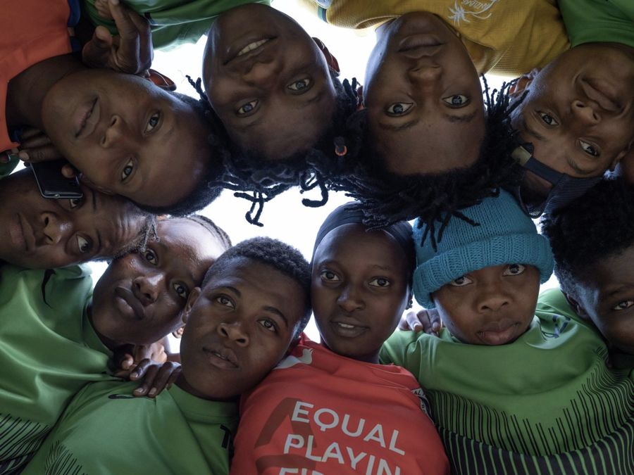 Zanzibar Girls Football Team, Zanzibar, Tanzania: a team in green shirts huddled in a circle, looking down into the camera. Photograph by Marcus Vallance.