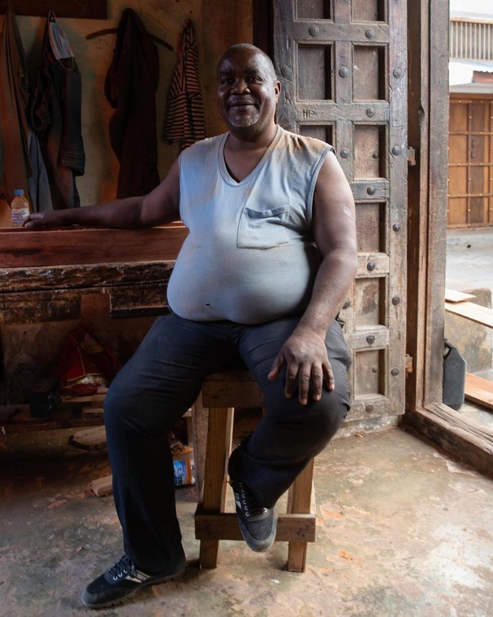 Carpenter, Zanzibar, Tanzania: a man seated on a stool beside a carved wooden door. Photograph by Marcus Vallance.