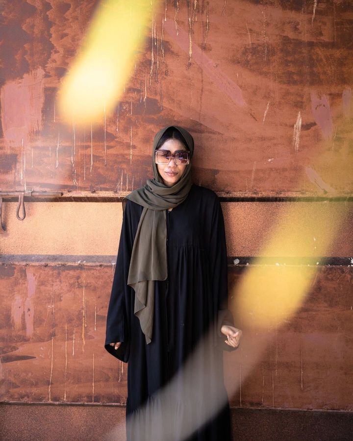 Aisha, Zanzibar, Tanzania: a woman standing against a rust-orange wall, with warm light flare. Photograph by Marcus Vallance.