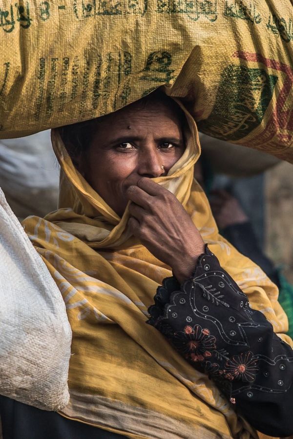 Portrait of a Woman, Kutupalong Refugee Camp, Bangladesh: a woman in a yellow headscarf carrying a sack on her head. Photograph by Marcus Vallance.