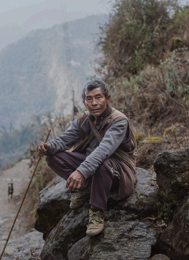 Portrait of a Man, Annapurna, Nepal: a man seated on a rock on a misty hillside. Photograph by Marcus Vallance.