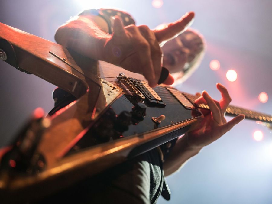 Tim Wheeler, London, UK: a guitarist seen from below the neck of his guitar, stage lights behind. Photograph by Marcus Vallance.