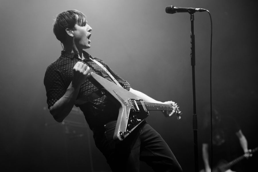 Tim Wheeler, The Roundhouse, London, UK: black and white live photograph of a guitarist leaning back from the microphone mid-shout, playing a Flying V guitar. Photograph by Marcus Vallance. From the postcard set sold by Ash.