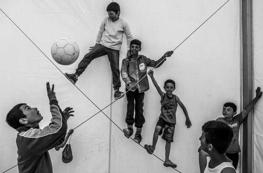 Kids Playing Football, Greece: black and white photograph of boys playing football against a white tent. Photograph by Marcus Vallance.