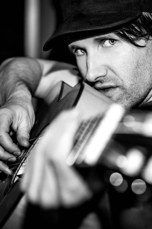 Tim Wheeler, Rome, Italy: black and white portrait of a man in a hat holding a guitar. Photograph by Marcus Vallance.