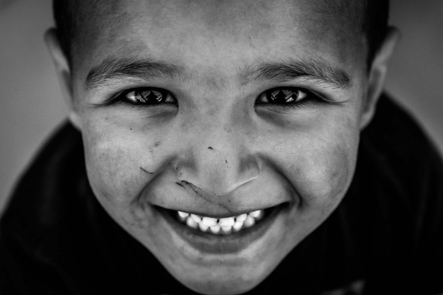 Mohammed, Idomeni, Greece: black and white close portrait of a boy grinning up at the camera. Photograph by Marcus Vallance.
